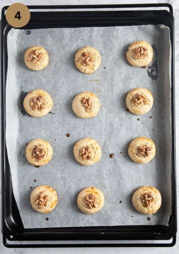 baked chinese cookies with walnuts on a baking sheet lined with white parchment paper.