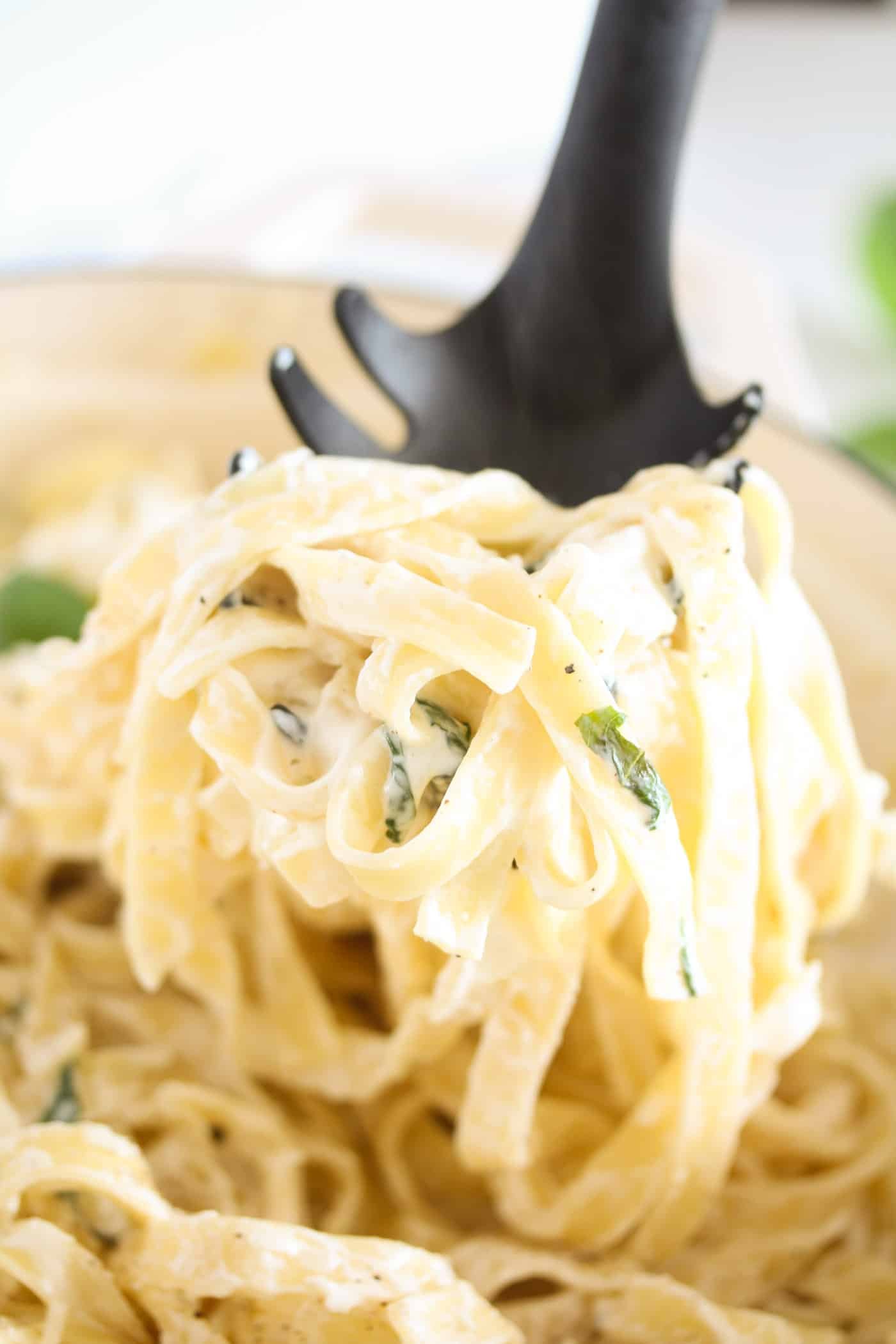 bunch of creamy noodles held by a black serving spoon.