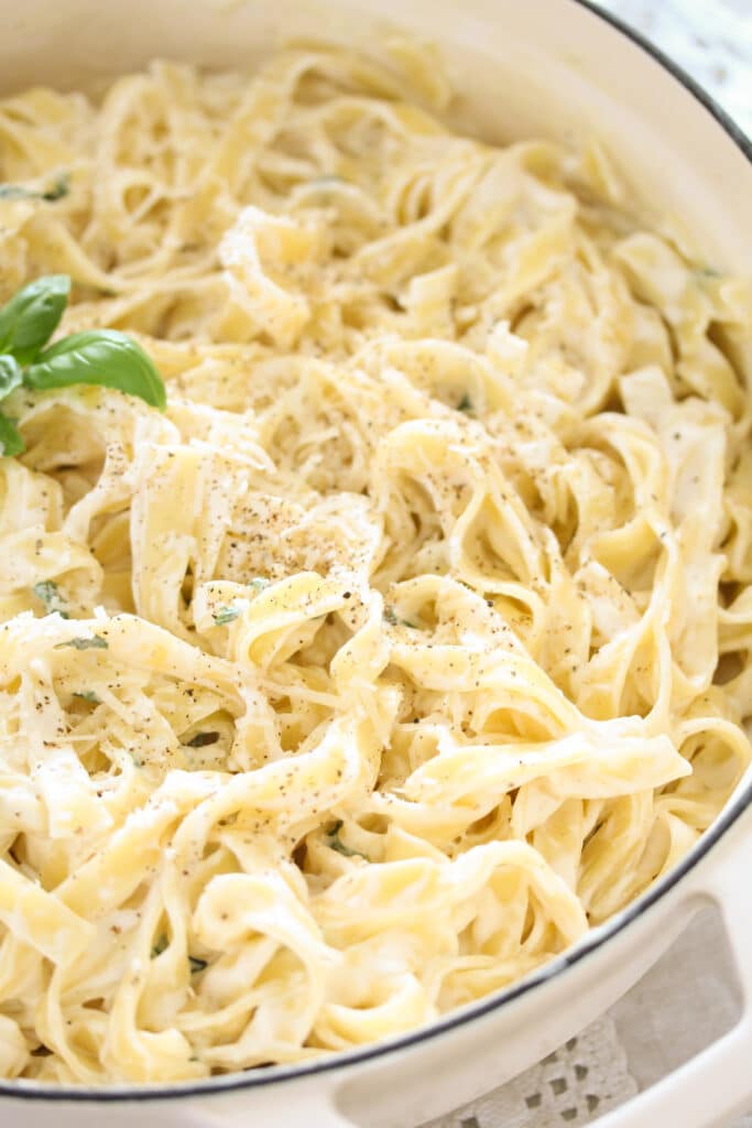 white dutch oven full of creamy pasta with cream cheese and garlic.