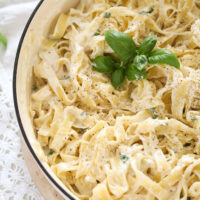 creamy tagliatelle with sauce and basil in a white pot.