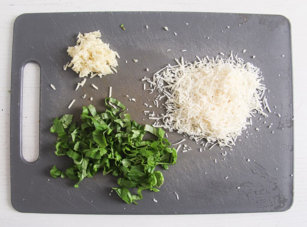 chopped basil, grated garlic and parmesan on a grey board.
