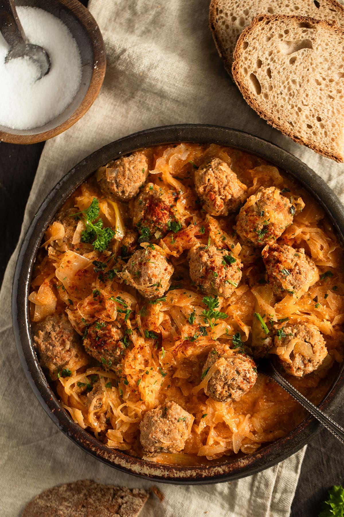 german meatballs cooked with sauerkraut, a few slices of bread and a bowl of salt on the table.