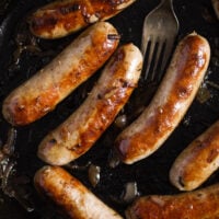 seven sausages in a cast iron pan with a fork.