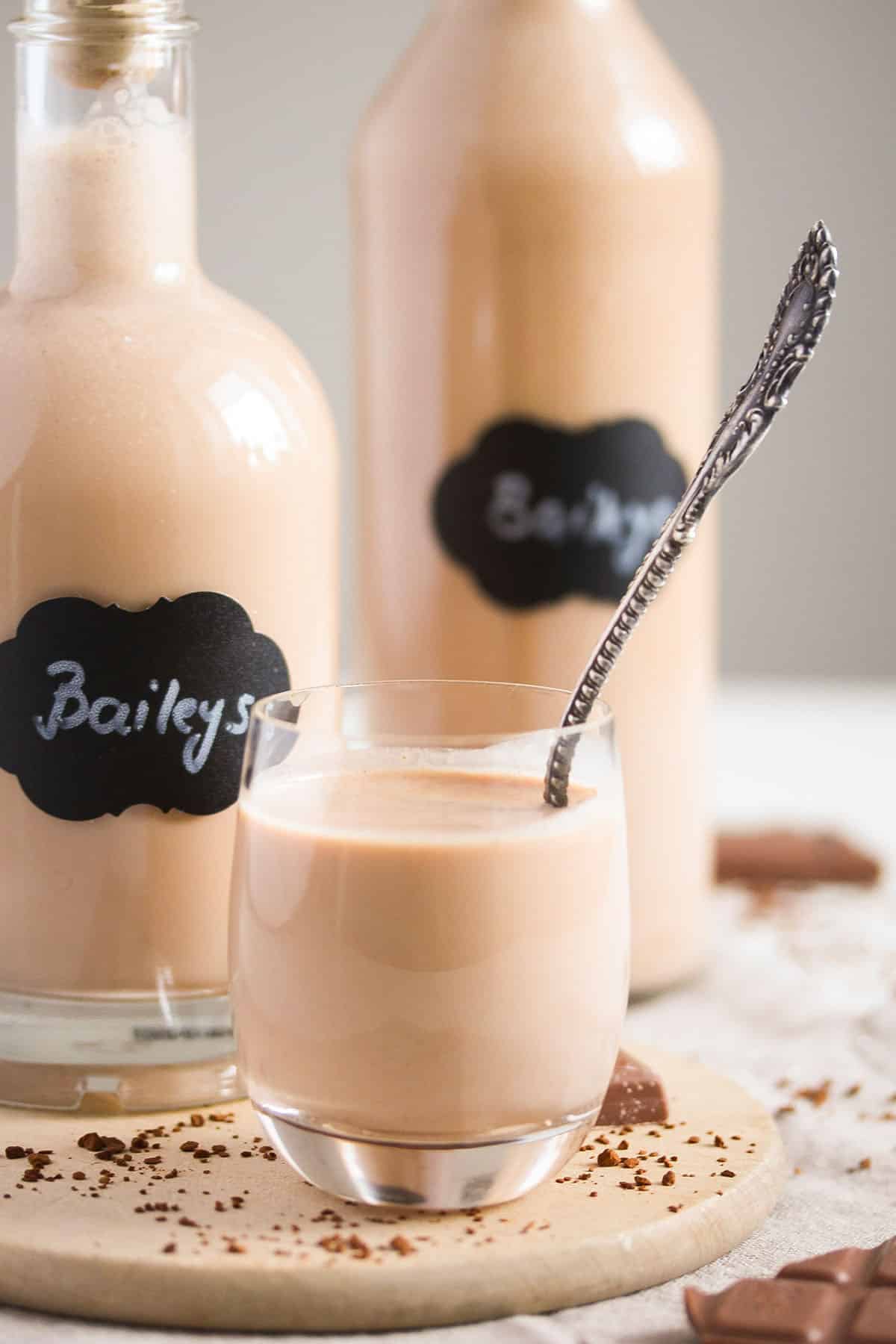 two bottles of homemade bailey's and a small glass full of it.