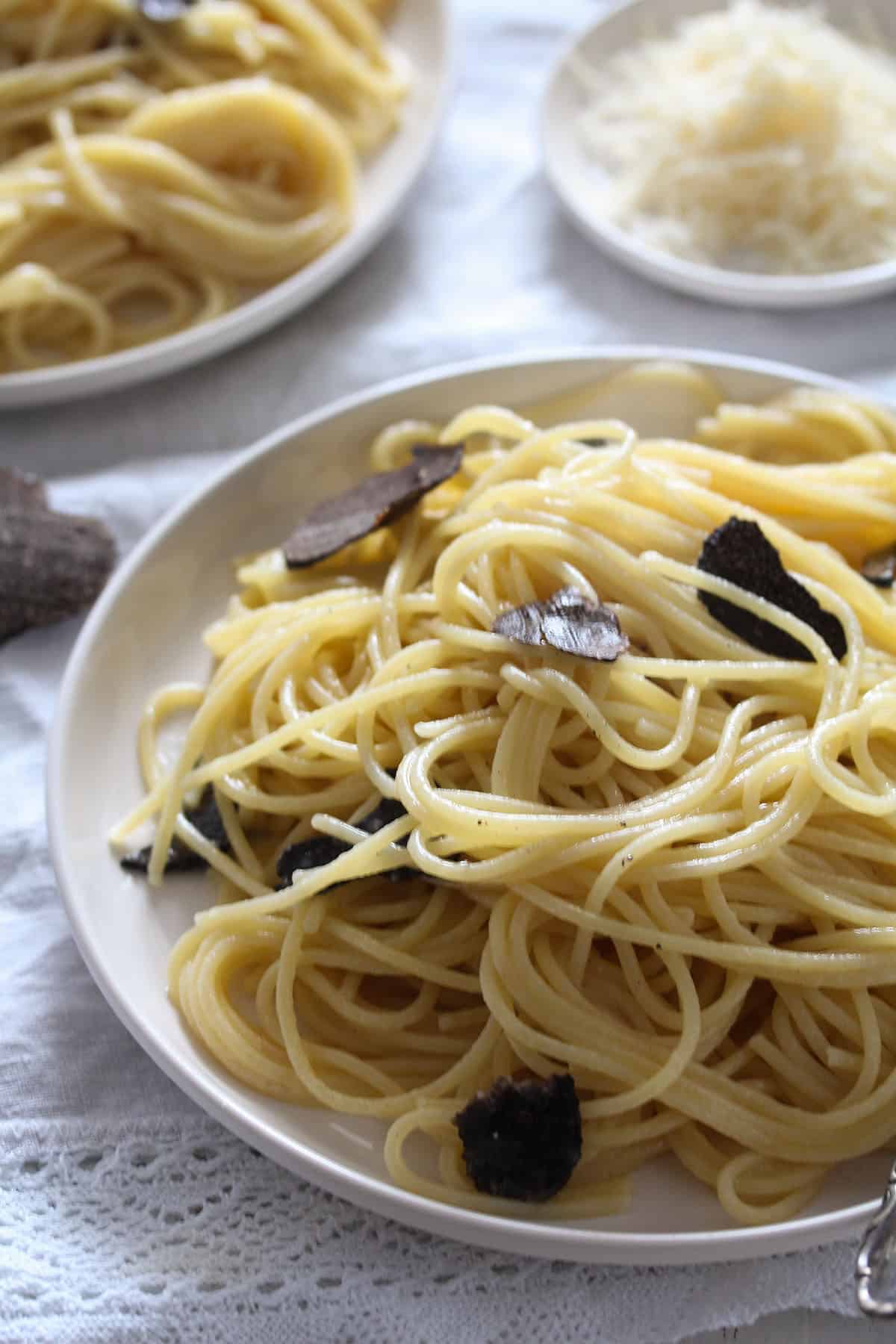 tangled pasta with black truffles on a plate, a bowl of parmesan behind it.