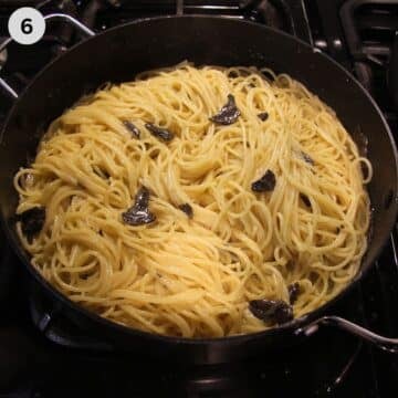 spaghetti mixed with butter sauce and shaved black truffles in large pan.