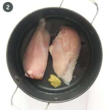 two frozen chicken breasts and some bouillon powder in a pot covered with water.