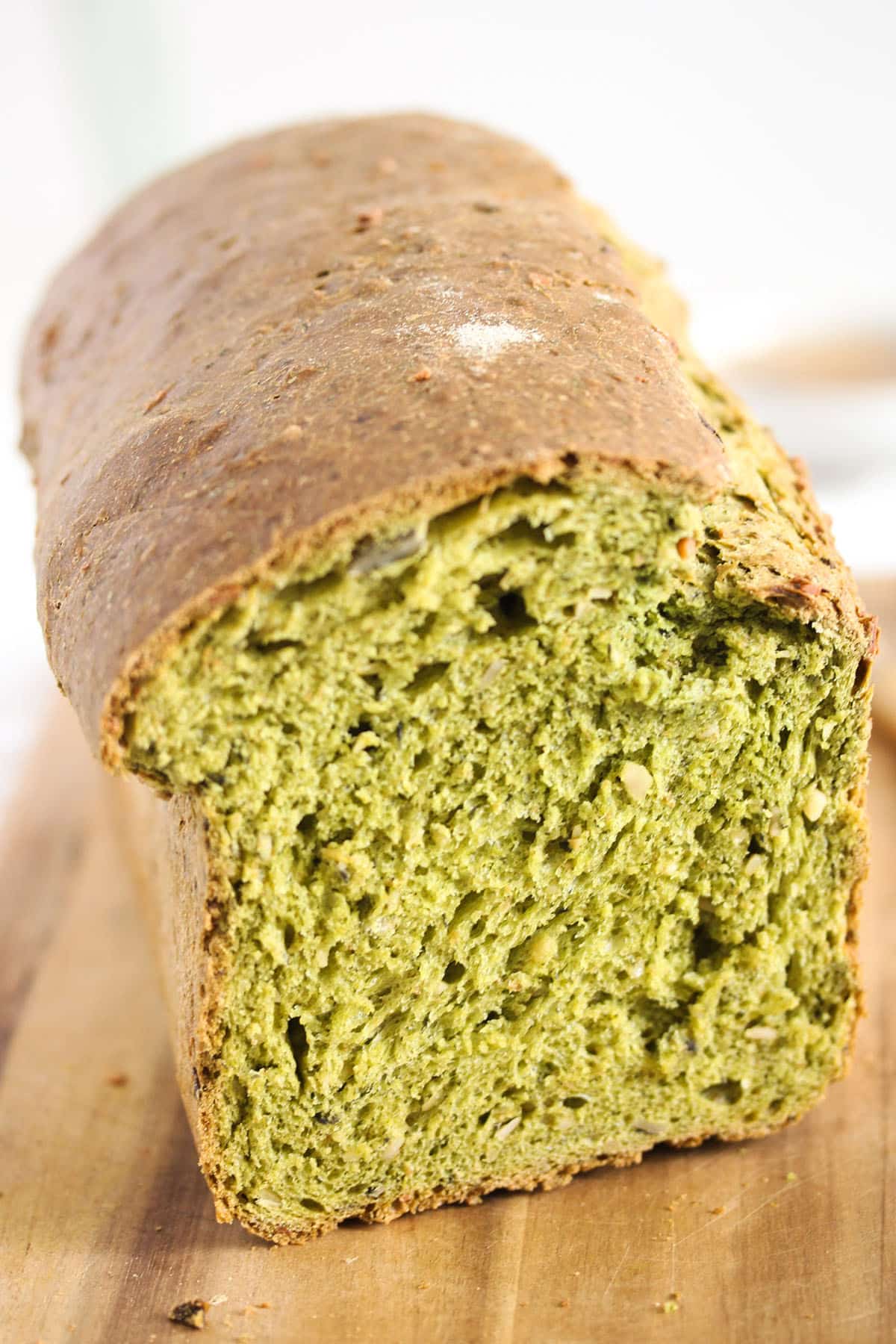one loaf of green spinach bread on a wooden cutting board showing the crumb.