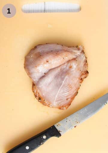 butterflied chicken breast and a meat mallet on a cutting board.