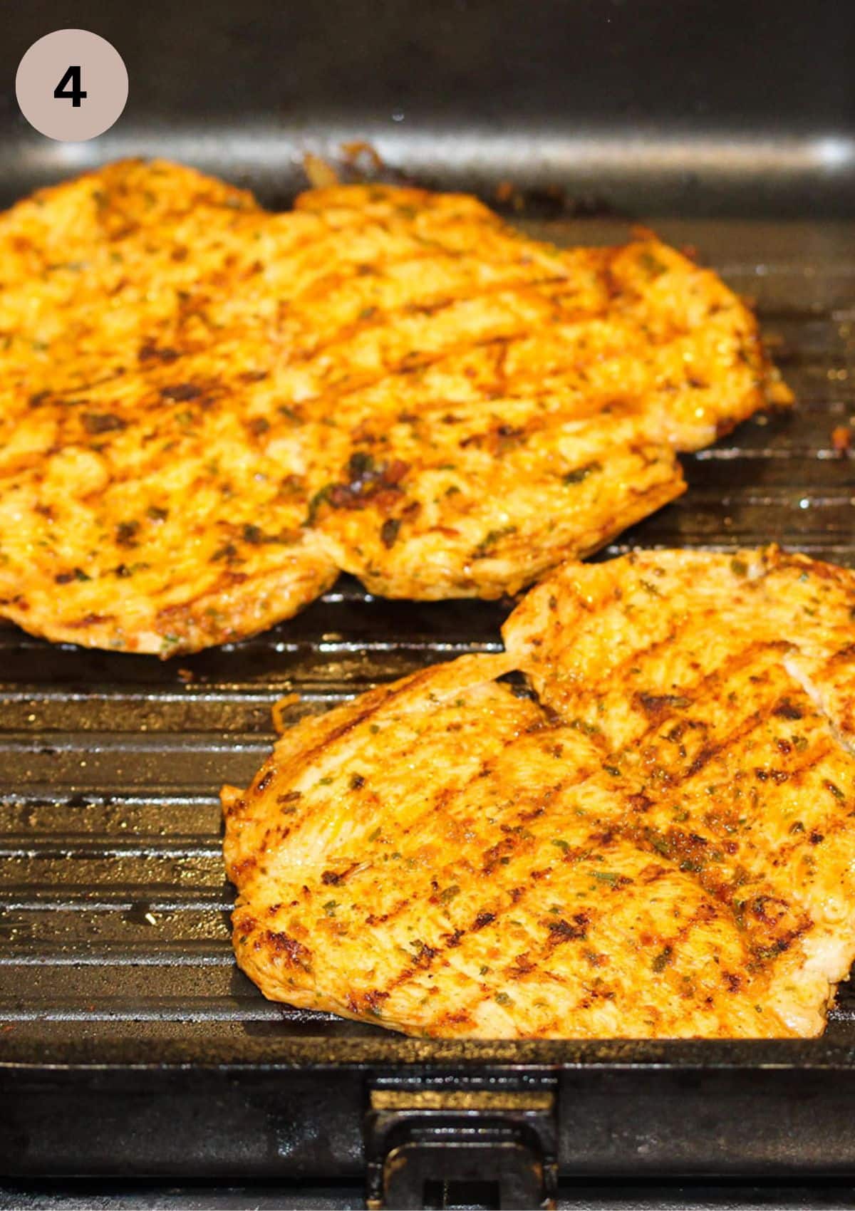 two pieces of butterflied chicken breast cooking in a grill pan.