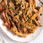 dutch oven pork butt shredded on a platter and drizzled with sauce.