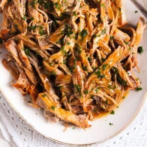 dutch oven pork butt shredded on a platter and drizzled with sauce.