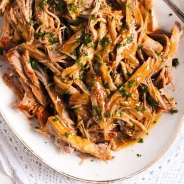 dutch oven pork butt shredded on a platter and drizzled with sauce.