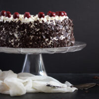 black forest gateau on a platter decorated with cherries.