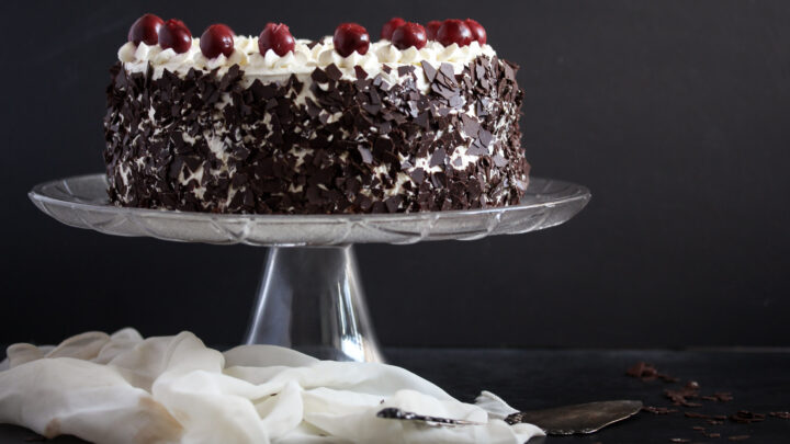 black forest gateau on a platter decorated with cherries.