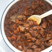 close up irish stew in dutch oven with a wooden spoon stirring it.