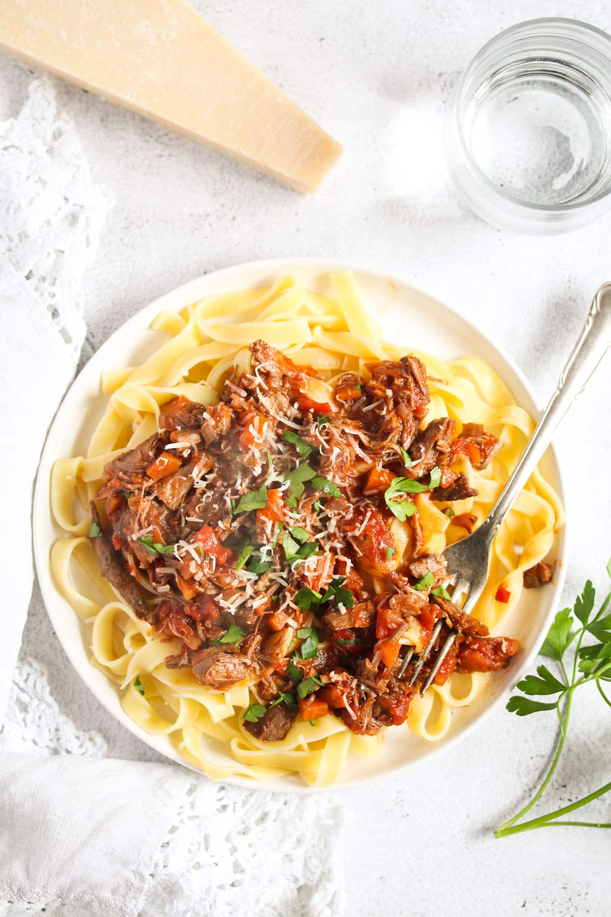leftover lamb ragu served over wide pasta and a piece of parmesan beside it.