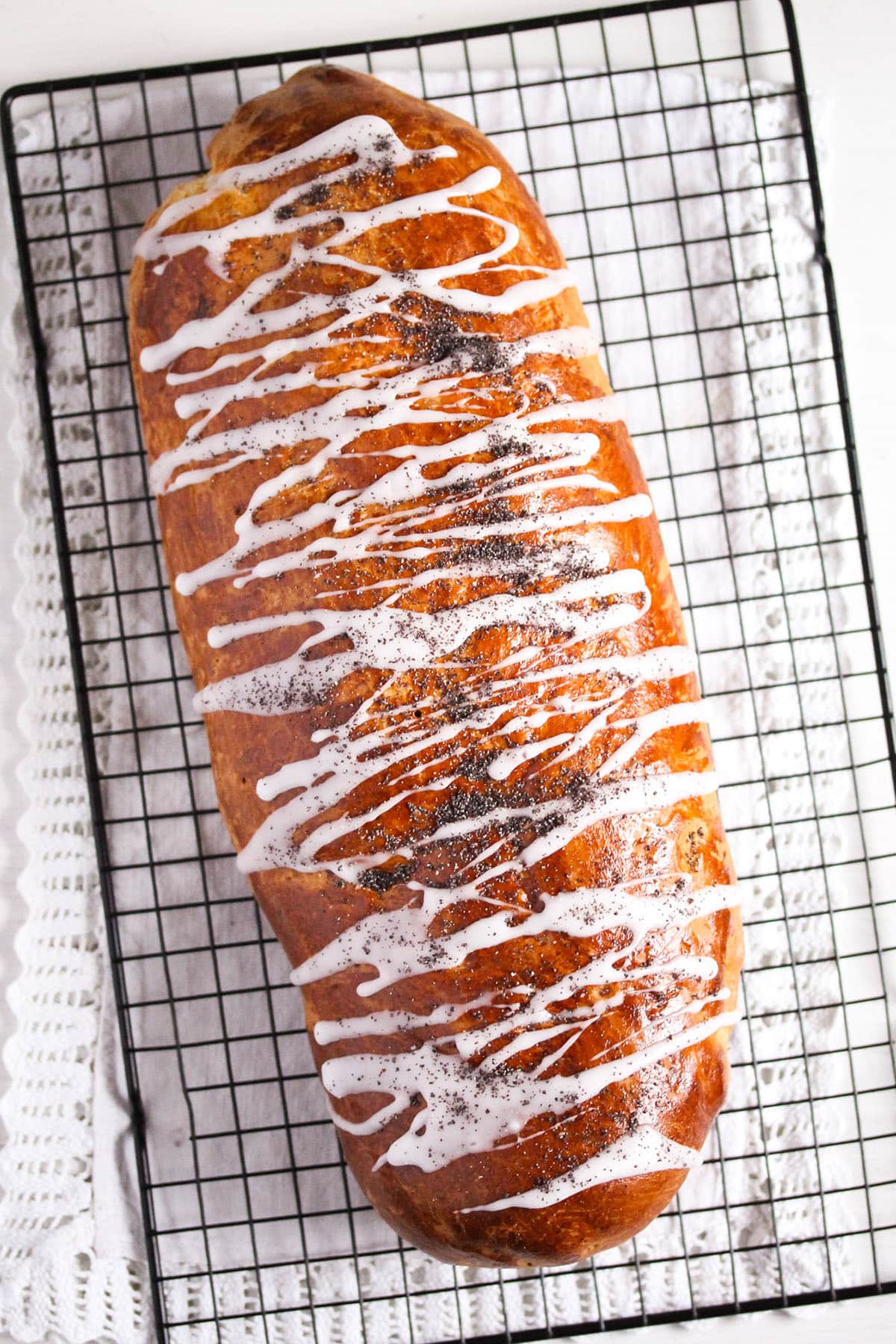 one polish roll drizzled with powdered sugar glaze on a wire rack.