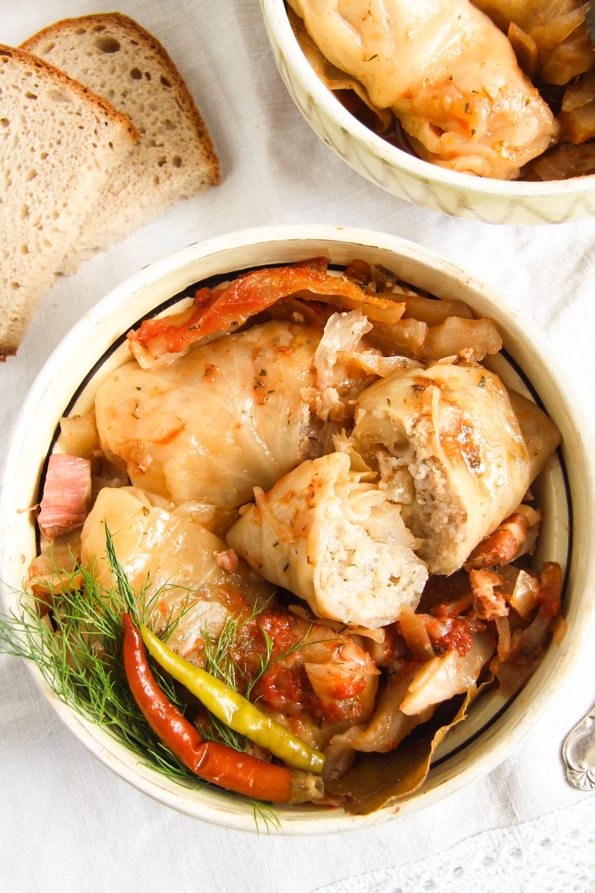 romanian sarmale cut to show the filling served with pickled hot peppers in a rustic bowl.