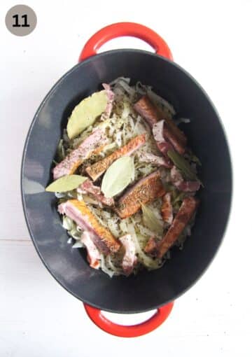 dutch oven containing chopped cabbage, bay leaves and smoked pork ribs.