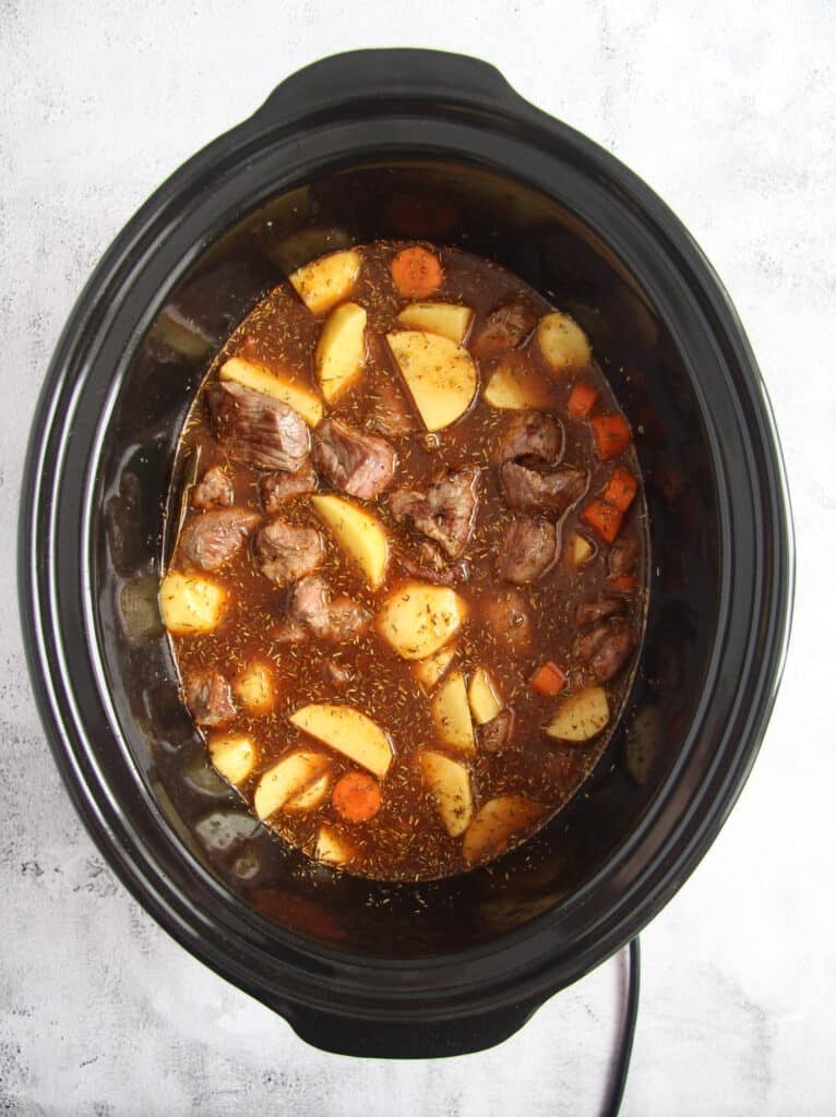 slow cooker full of uncooked potatoes, meat and sauce.
