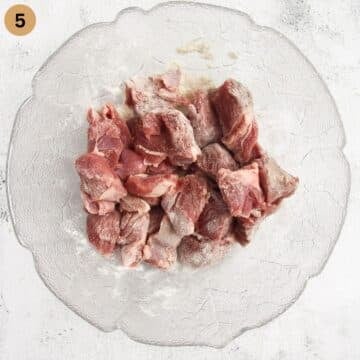 flouring lamb pieces in a bowl.