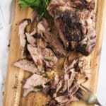 overhead picture of lamb roast being served on a wooden board.