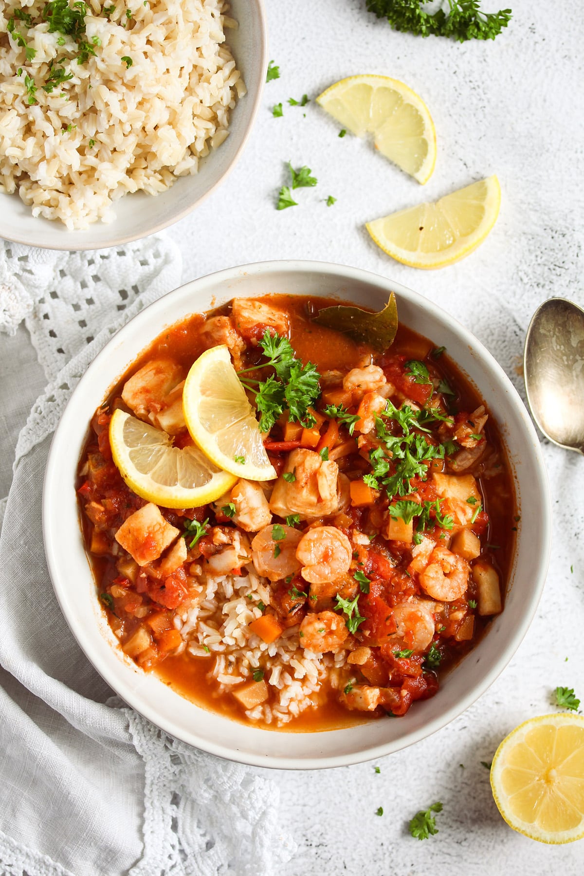 bowl of fish stew sprinkled with parsley and a bowl of rice beside it.