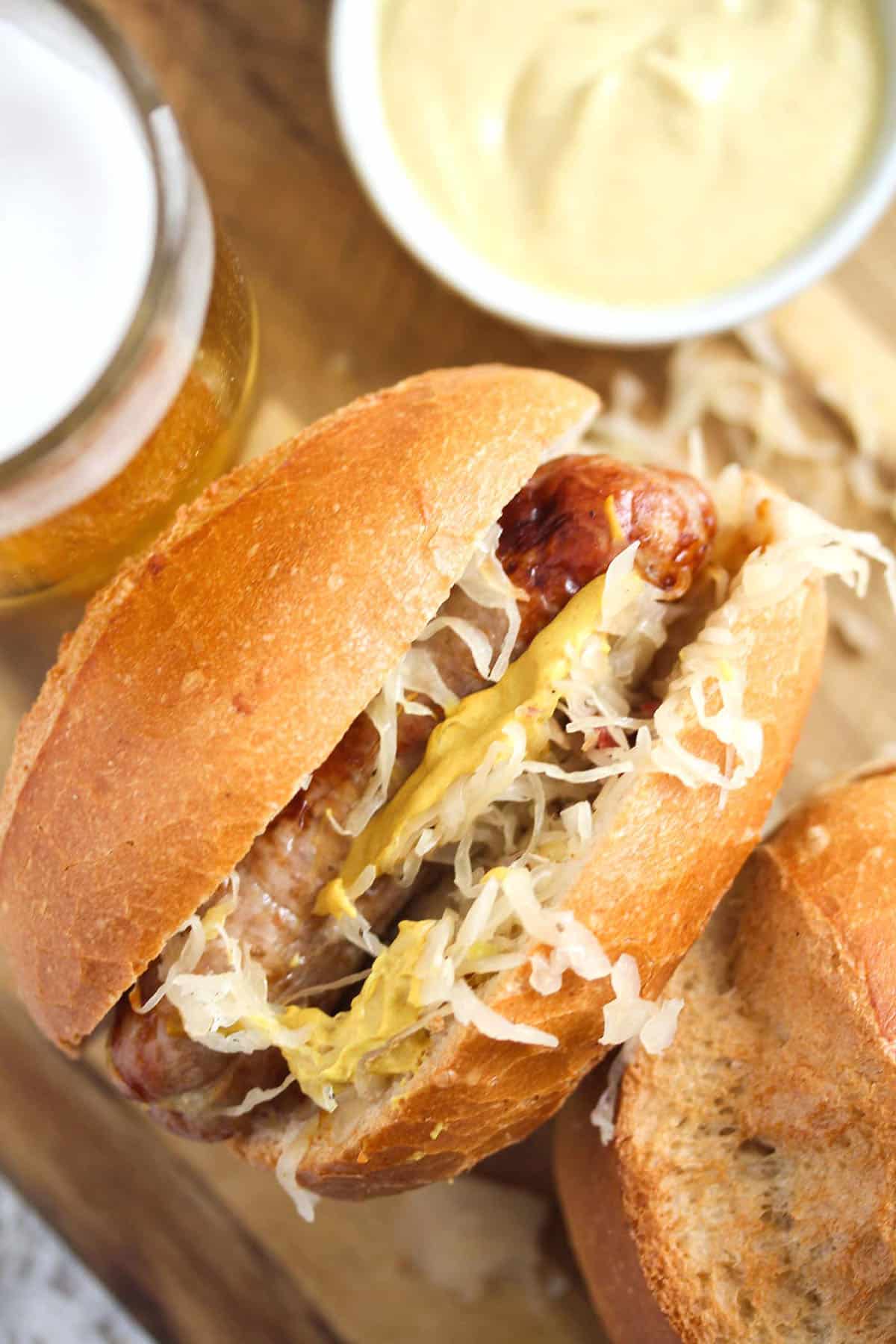 air fryer brat in a bun with sauerkraut, a bowl of mustard beside it.