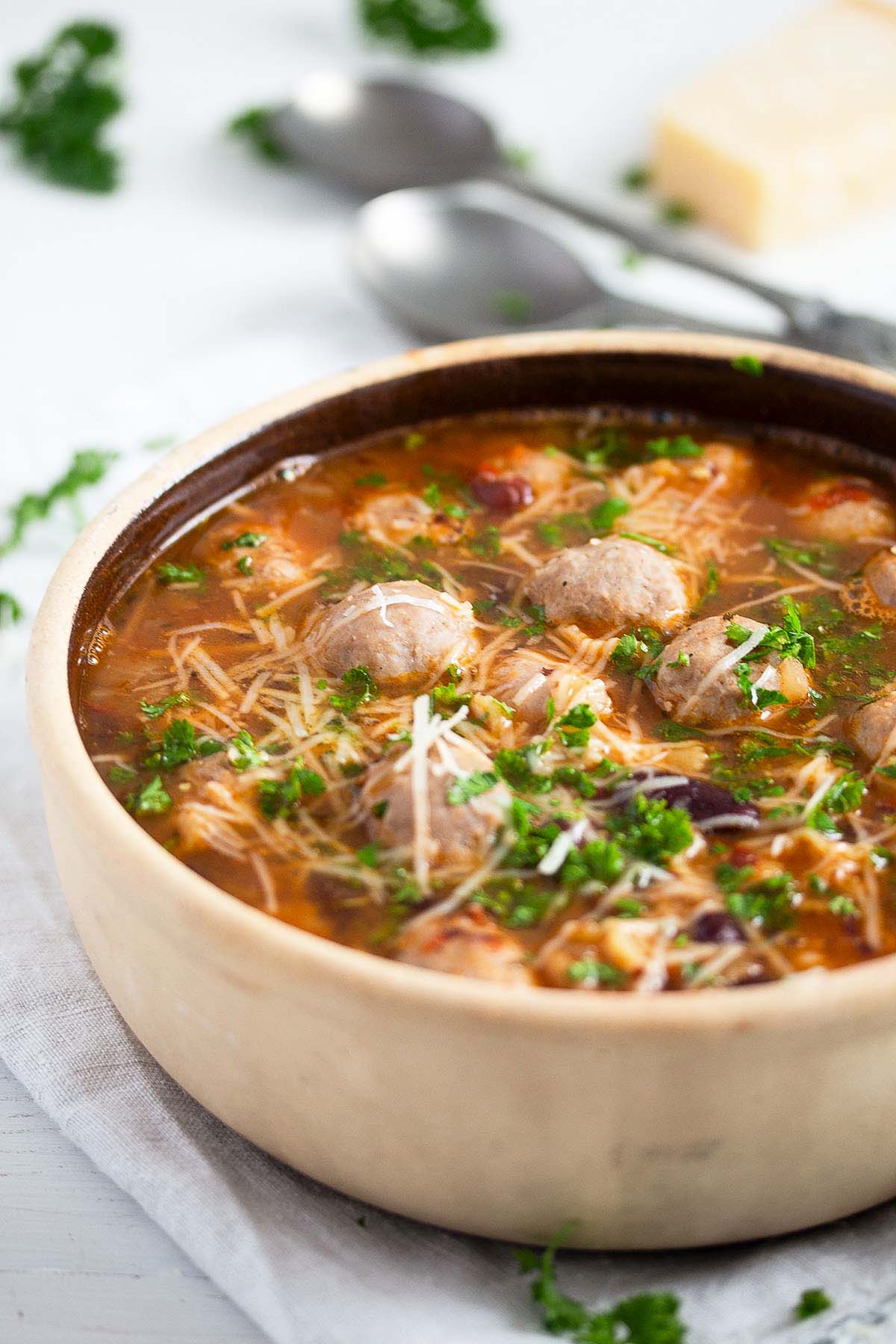 soup with meatballs made from bratwurst, beans, pasta and parmesan in a pot.