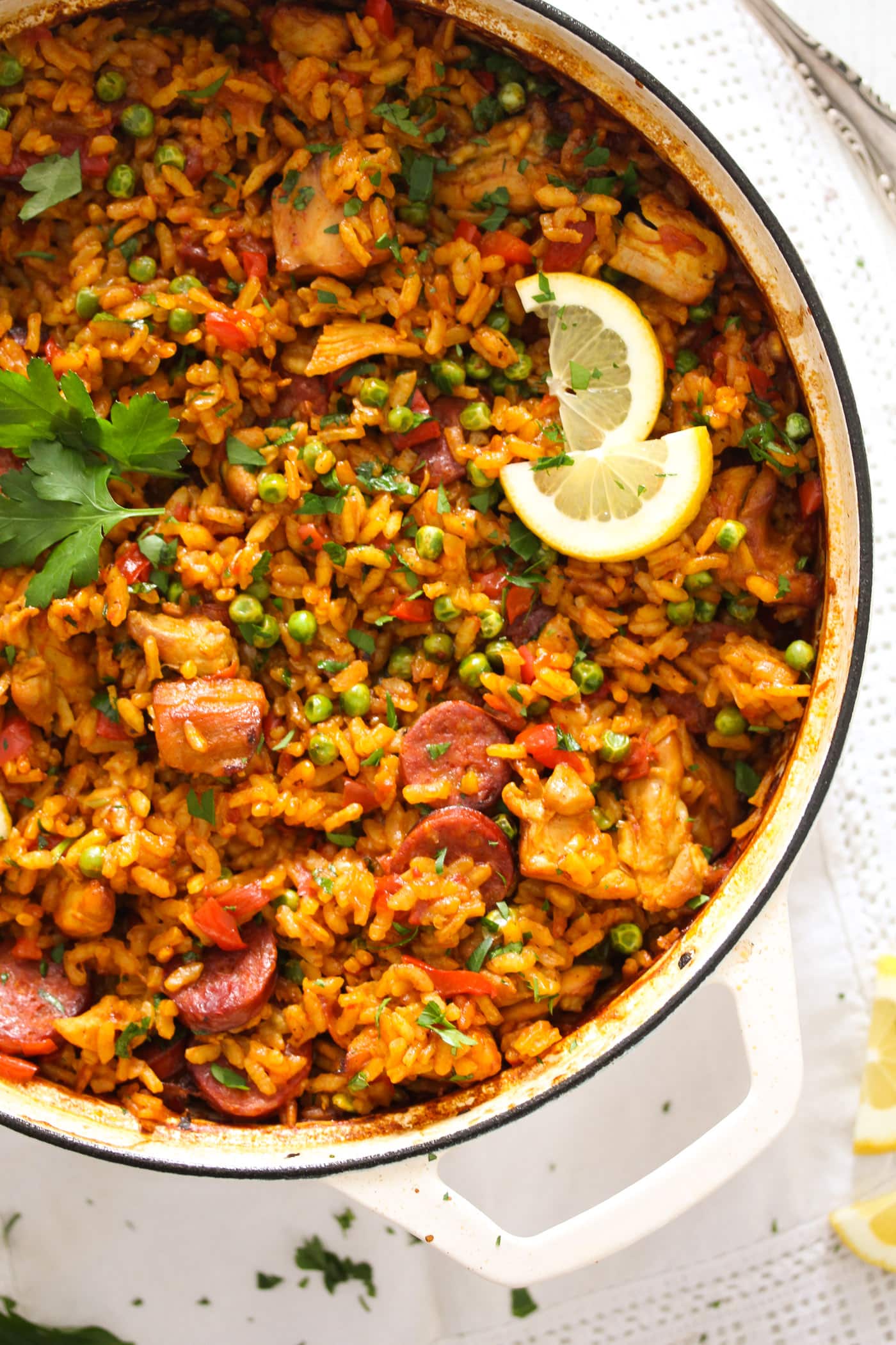 chorizo chicken paella garnished with parsley and lemon wedges in a white pot.