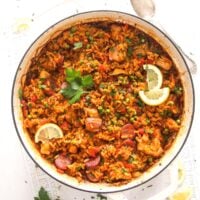 chorizo chicken paella garnished with parsley and lemon wedges in a white pot.