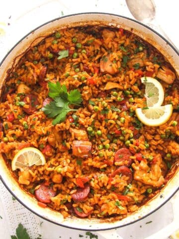 chorizo chicken paella garnished with parsley and lemon wedges in a white pot.