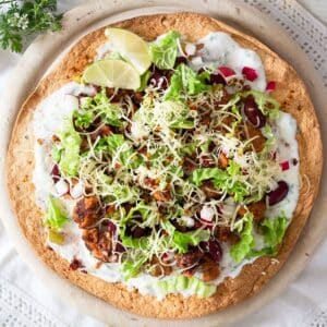 one large chorizo tostada topped with yogurt, beans, lettuce, cheese and lime wedges.