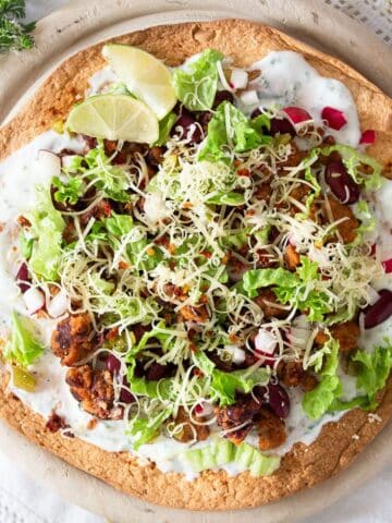 one large chorizo tostada topped with yogurt, beans, lettuce, cheese and lime wedges.