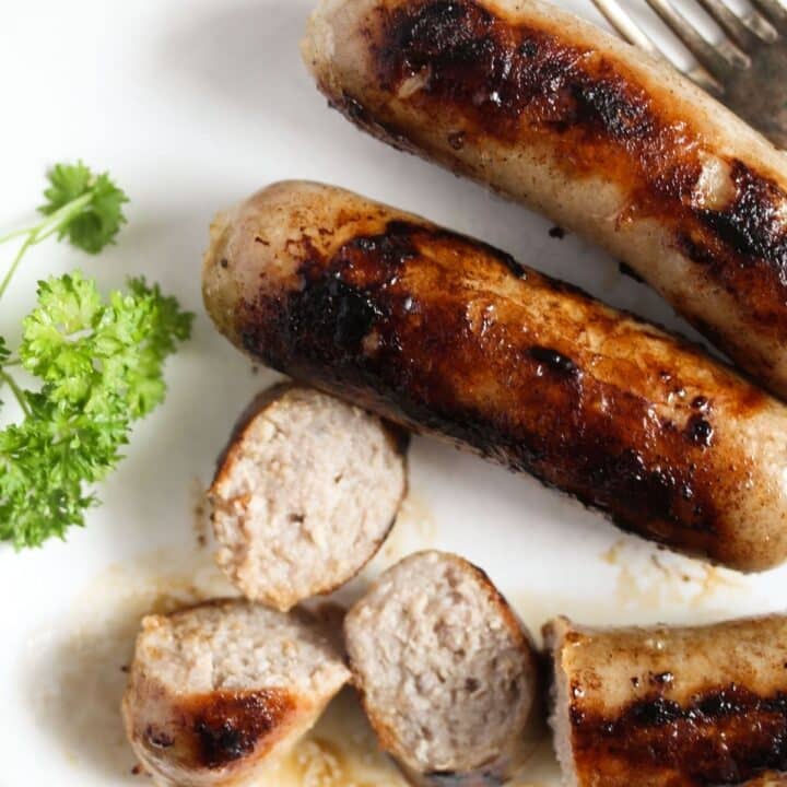 two whole and two sliced cooked brats cooked from frozen on a plate.