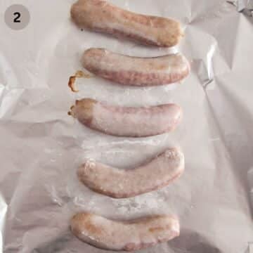 five half cooked sausages on a baking sheet.