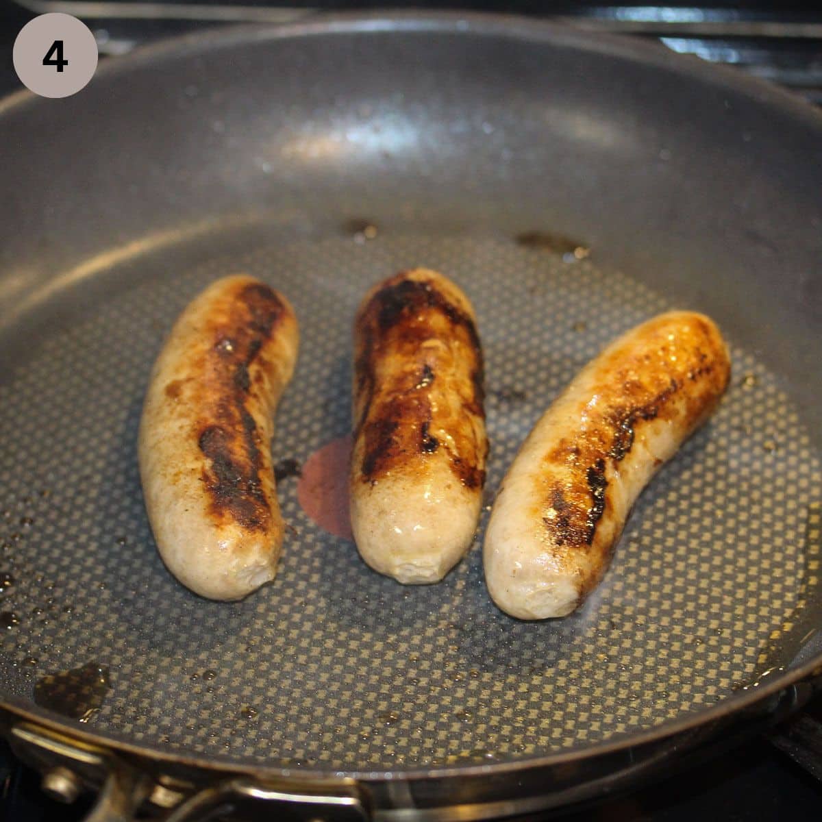 three browned brats in a nonstick pan.