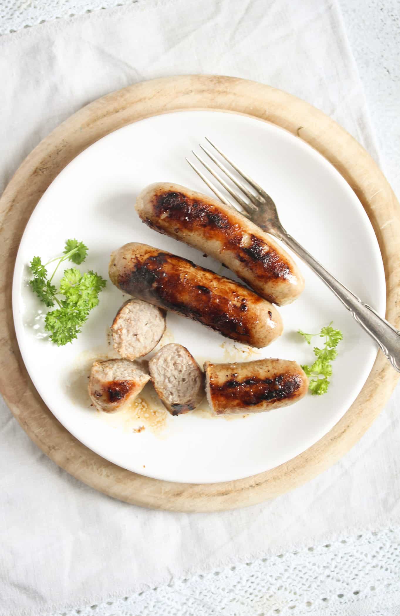 small white plate with three brown sausages and a fork.