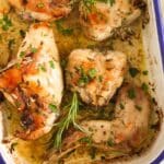 roasted rabbit pieces and rosemary sprigs in cooking juice in a pan.