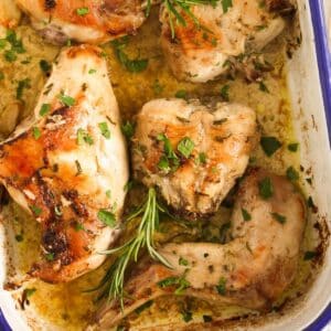 roasted rabbit pieces and rosemary sprigs in cooking juice in a pan.