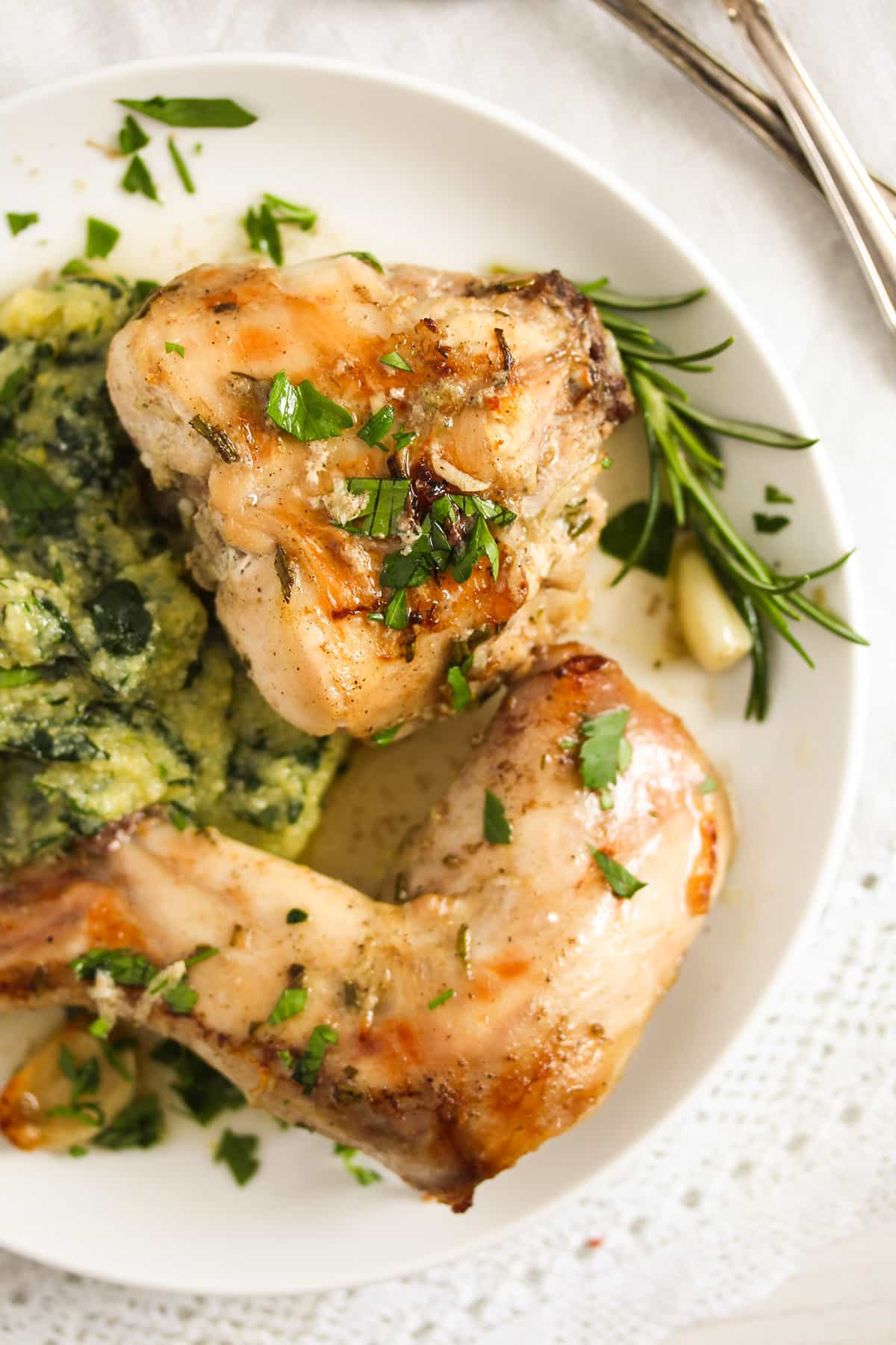 two pieces of oven baked rabbit and rosemary sprigs on a plate.