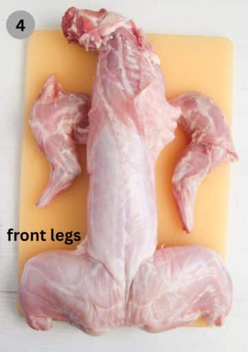a whole uncooked rabbit on a cutting board.