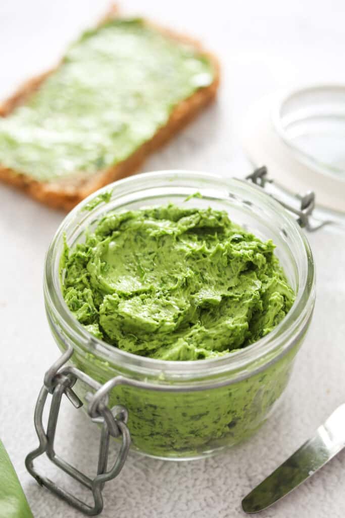 small jar with wild garlic butter and a slice of bread behind.