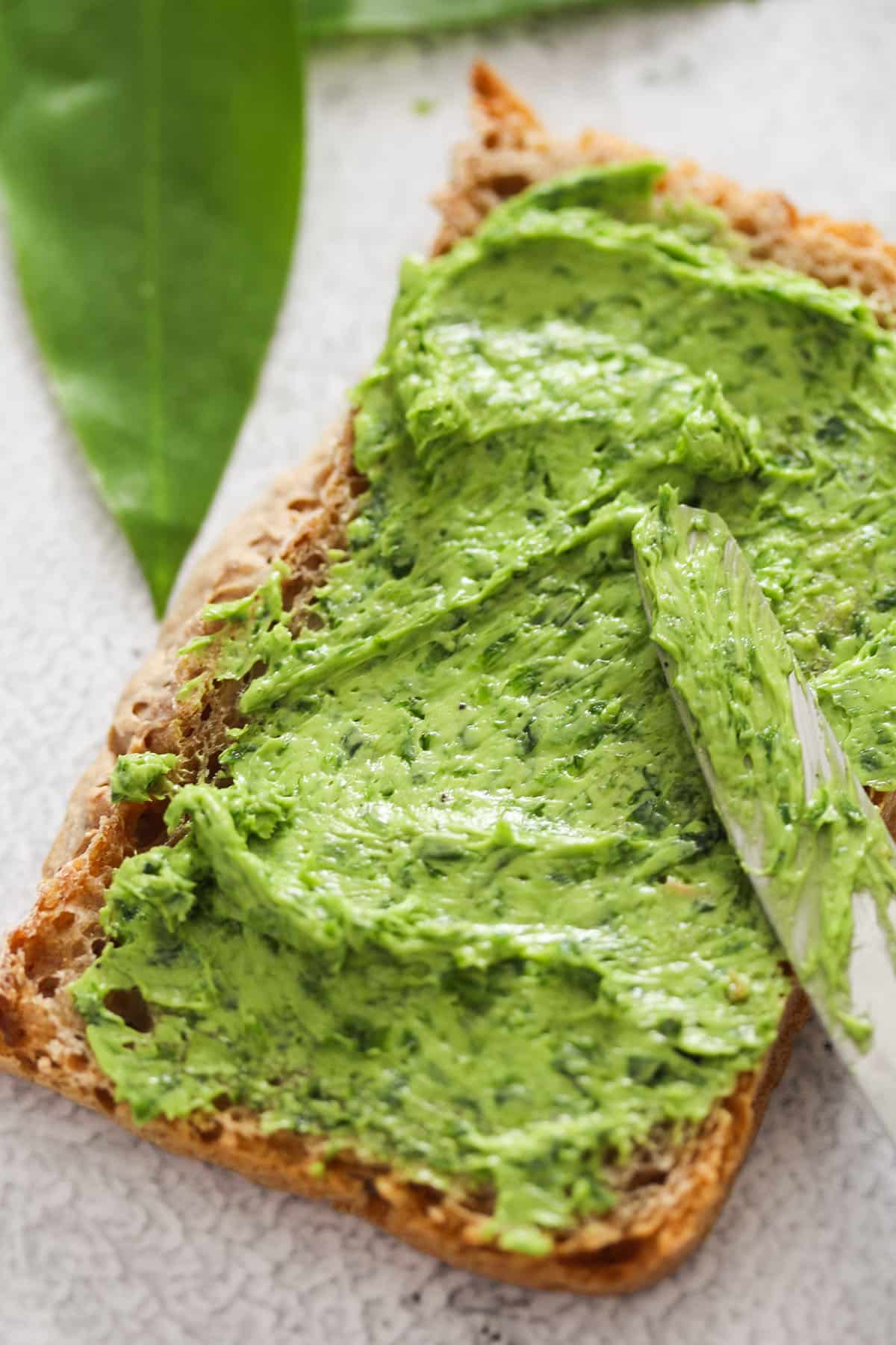 thickly spreading wild garlic butter on a pieces of bread with a knife.