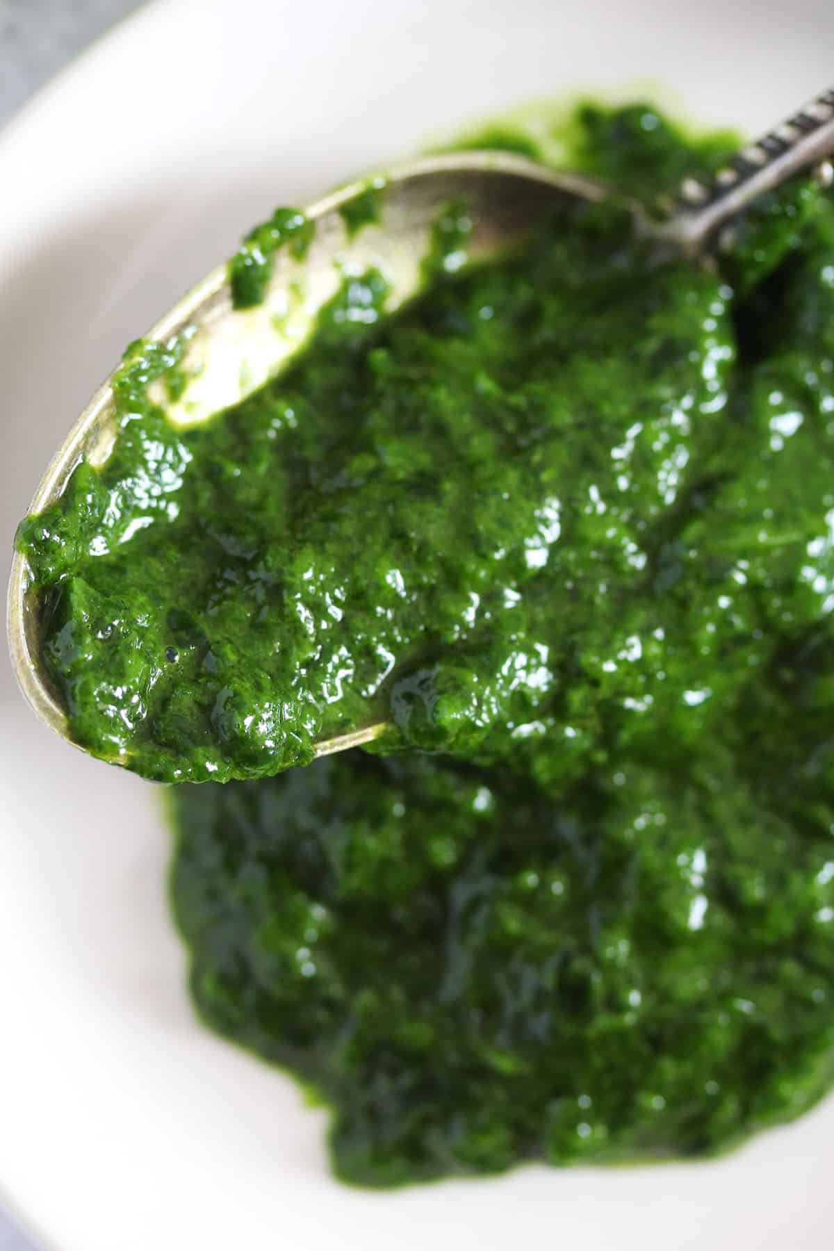 thick wild garlic paset with oil and salt on a spoon over a plate.