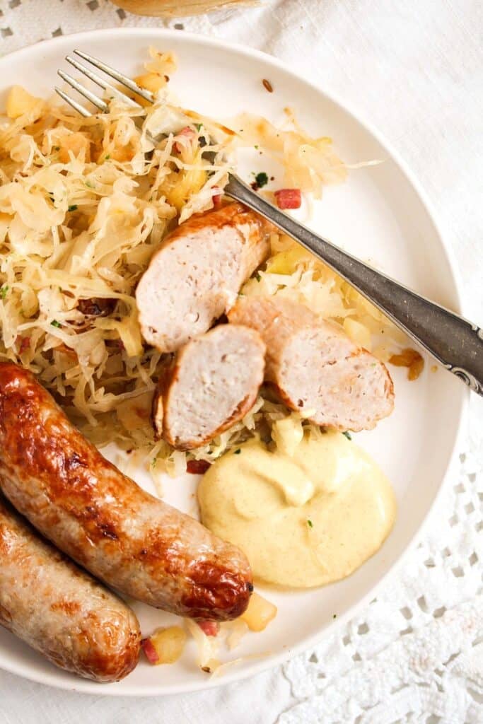overhead view of a plate with cooked sauerkraut, bratwurst and mustard.