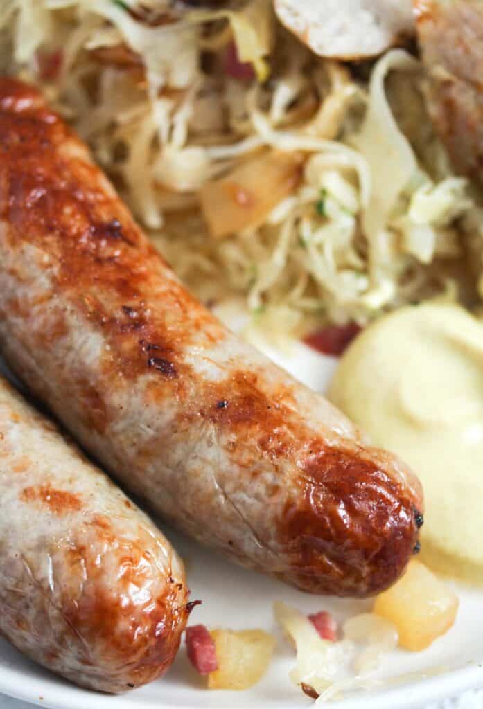 two brats and sauerkraut on a plate served with mustard.