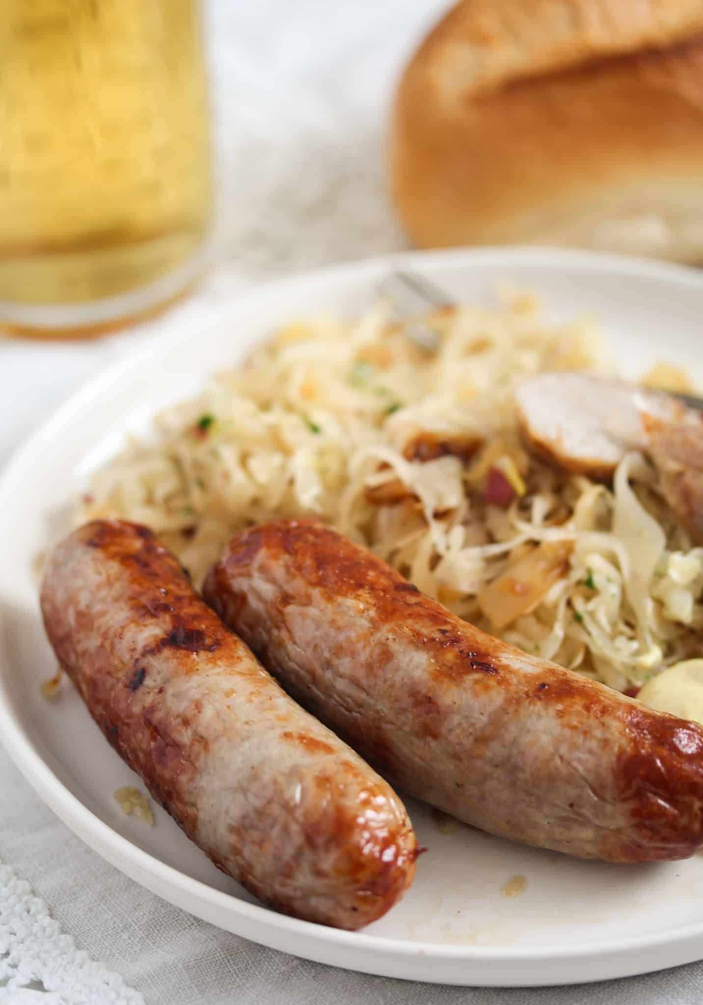 two sausages on a bed of sauerkraut with a bread roll and a glass of beer behind.