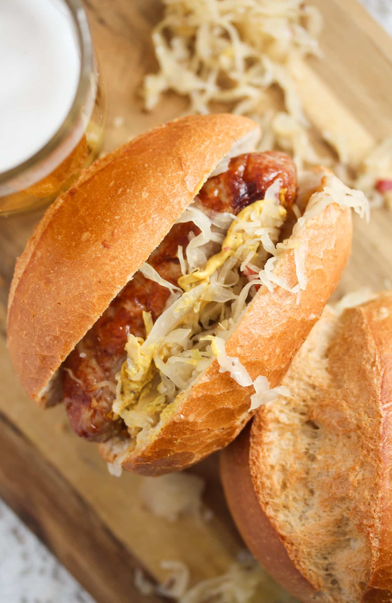 german bread roll stuffed with kraut and bratwurst on a wooden board with a glass of beer.